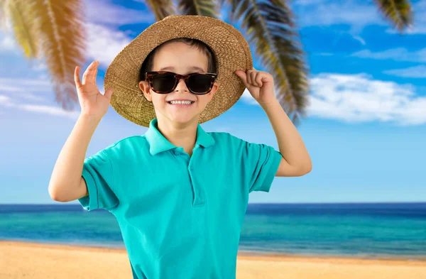 stock image Child on vacation wearing blue t-shirt hat sunglasses at tropical beach happy face smiling and looking at the camera. Positive person