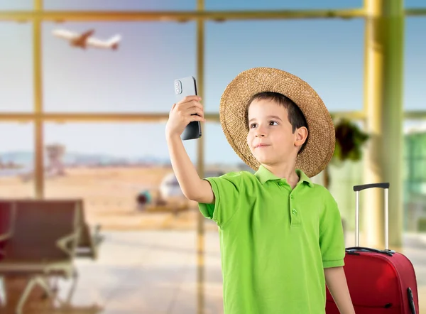 空港でスマートフォンによる帽子と笑顔の子供 — ストック写真