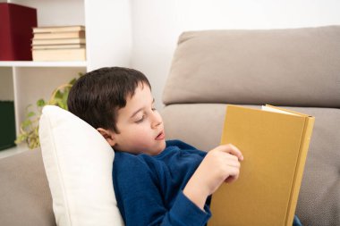 Kanepede yatarken kitap okuyan sevimli bir çocuğun portresi, evde eğitim konsepti ve okula geri dönüp uzayı kopyalamak.