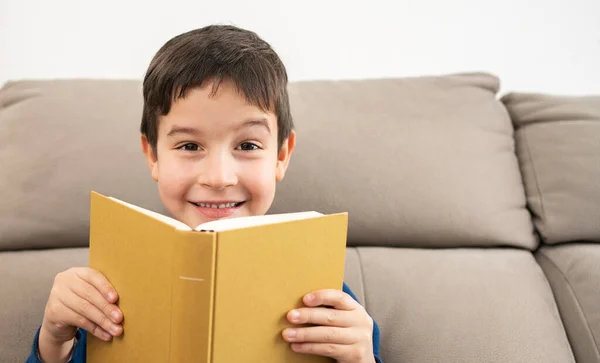 Chłopiec Siedzi Kanapie Trzyma Książkę Przed Twarzą Salonie Przestrzenią Kopiowania — Zdjęcie stockowe