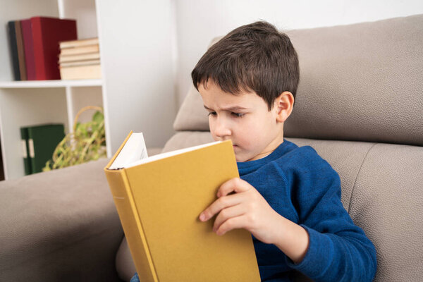 Child wearing reading book while sitting on couch, homeschooling concept and back to school and copy space