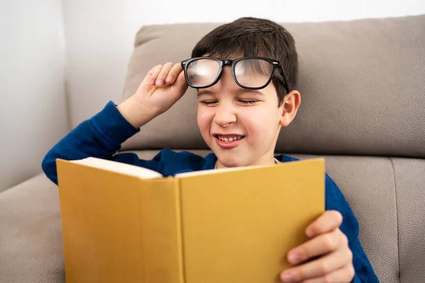 Child suffering eyes strain trying to read a book at living room