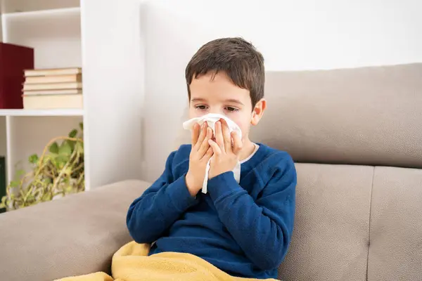 冬の自宅でソファーに座っているインフルエンザ症状に苦しむワイプで子供が吹く ロイヤリティフリーのストック写真