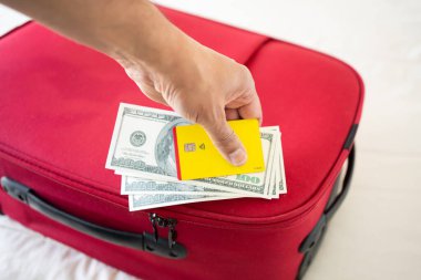 Tanınmayan bir iş adamı kırmızı bir bavulda Amerikan doları ve sarı kredi kartı gösteriyor.