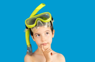 Şnorkel maskeli ve şnorkeli olan dalgın çocuk, mavi arka planda izole edilmiş bir şekilde fotokopi alanına bakıyor, komik çocuk dudakları, bir tür şaka yaparken parmaklarını ağzının kenarında tutuyor, şnorkelle yüzüyor., 