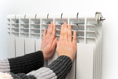 Kadın ellerinin ısıtması merkezi radyatör termostatına değince enerji tasarrufu soğuk hava sıcaklığını kapatır. Yurt içi ısınma maliyet artışı kontrol ev harcamaları para ekonomisini azaltır