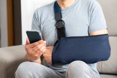 Kırık kollu, askı takan ve evde akıllı telefon kullanan erkek ellerini kapat.