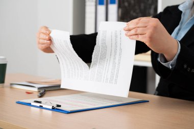 Close-up of the hands of a businesswoman tearing up the signed contract document sitting at a desk in the office clipart