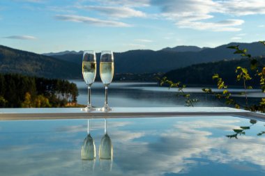 Havuzun kenarında iki kadeh şampanya dağların arka planında, göl, bulutlu mavi gökyüzü