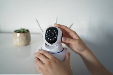 Orta kesime ve elinde güvenlik kamerası olan kimliği belirsiz beyaz kadının ellerine yaklaş. Odada durmuş, mobilya kopyalama alanına ekipman yerleştiriyor ve düzenliyor.