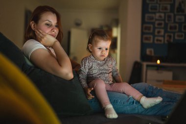 Küçük beyaz çocuk, küçük kız bebek anne ve kız geceleri karanlık bir odada kanepe yatağında oturup çizgi film ya da dizüstü bilgisayar filmleri izliyorlar.