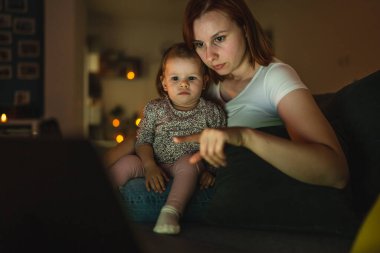 Küçük beyaz çocuk, küçük kız bebek anne ve kız geceleri karanlık bir odada kanepe yatağında oturup çizgi film ya da dizüstü bilgisayar filmleri izliyorlar.