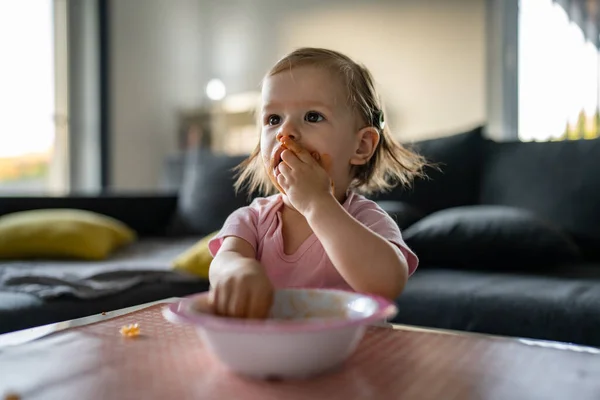 소녀는 아장아장 집에서 테이블에서 식사를 있었고 얼굴에 더러운 소세지를 바르고 — 스톡 사진