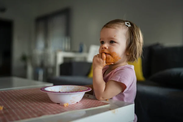 소녀는 아장아장 집에서 테이블에서 식사를 있었고 얼굴에 더러운 소세지를 바르고 — 스톡 사진