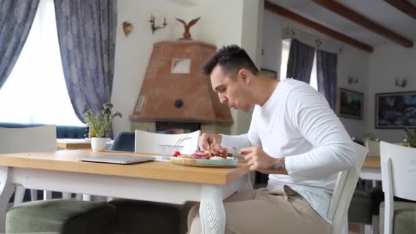 一位年轻的白人男性男子坐在餐馆的餐桌旁 手里拿着汉堡和法国火锅薯片 在现实生活中独自吃饭 — 图库视频影像