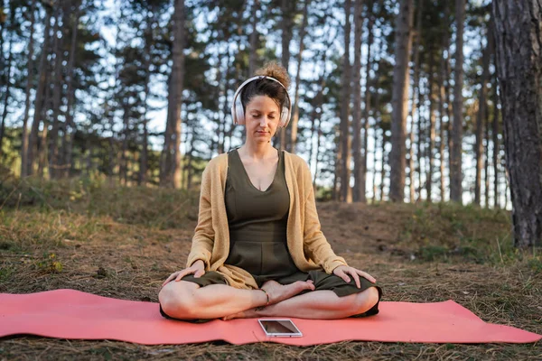 stock image One woman young adult caucasian female sitting alone in the park or forest in nature holding adjusting headphones preparing for online guided meditation self-care mental balance practices concept