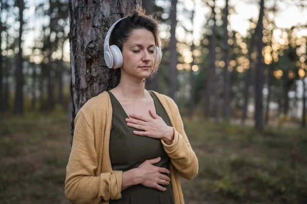 公園や森の中に一人で立つ若い大人の白人女性の一人ヘッドフォンでガイド付き瞑想セルフケア症状の練習精神的な感情的なバランスの概念を準備 — ストック写真