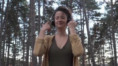 Genç yetişkin bir kadın, parkta ya da ormanda yalnız başına meditasyona hazırlanan kulaklıkları ayarlıyor. Kişisel bakım, zihinsel denge kavramını uyguluyor.