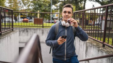 Genç, yetişkin bir erkek elinde kahve ve cep telefonuyla merdivenlerden çıkıyor. Turist ya da öğrenci fotokopi alanı.