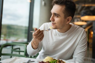 Genç, yetişkin, beyaz bir erkek halka açık bir restoranda masada oturuyor ve gerçek insanları yiyor.