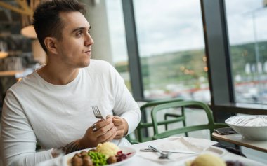 Genç, yetişkin, beyaz bir erkek halka açık bir restoranda masada oturuyor ve gerçek insanları yiyor.