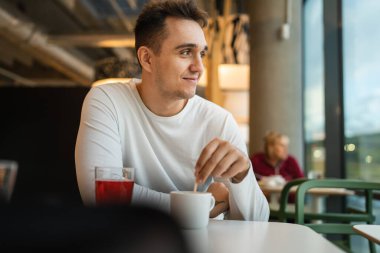 Genç, yetişkin, beyaz bir adam kafeteryada ya da restoranda tek başına oturuyor. Yan tarafa bakıyor, bir fincan kahve içiyor. Gerçek insanlar uzayı kopyalıyor.