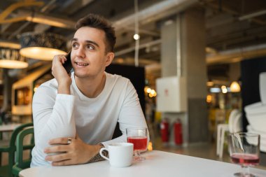 Genç yetişkin bir erkek kafeteryada ya da restoranda cep telefonuyla konuşuyor gerçek insanlar uzayı kopyalıyor.