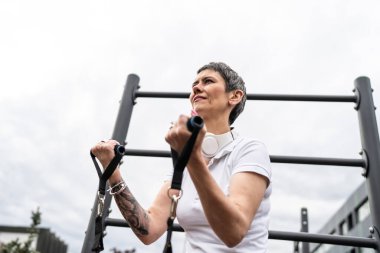 Bir kadın olgun ya da yaşlı, kauçuk elastik direnç bantlı beyaz kadın eğitimi. Açık spor salonunun spor salonundaki tüplerde. Sağlıklı yaşam tarzı konsepti.