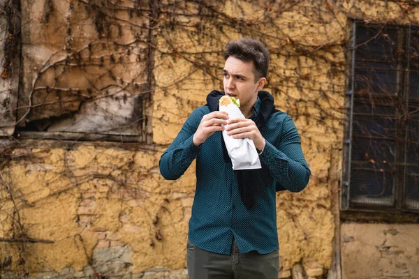 秋の春や冬の日に屋外に立つ1人の男古い壁の前で屋外を待っている間に足で食べるサンドイッチの観光客を保持実際の人々はスペースをコピーしますファーストフードの概念 — ストック写真