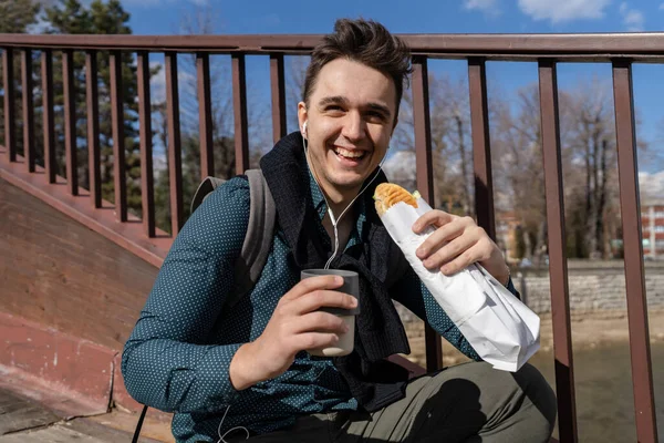 秋の春や冬の日に屋外の笑顔を立っている1人の男街や町で屋外に座っている間に食べるサンドイッチ観光客を保持実際の人々は スペースをコピーしますファーストフードの概念 — ストック写真