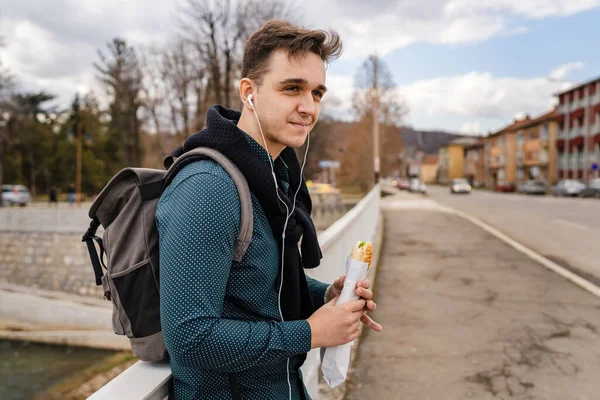 秋の春や冬の日に屋外に立つ1人の男街や町で屋外を歩いている間に足で食べるサンドイッチの観光客を保持する実際の人々は スペースをコピーしますファーストフードの概念 — ストック写真