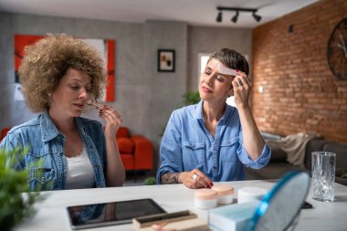 İki olgun yetişkin ve kıdemli bayan arkadaş güzellik ve cilt bakımı ürünleri kullanıyorlar gua sha jade yüz silindiri gerçek insanlar evlerinde yer kopyalıyorlar