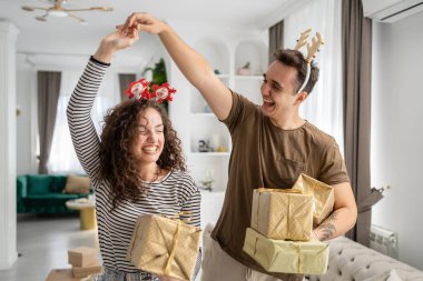 Erkek arkadaşı ya da kocası mutlu bir şekilde gülümserken elinde hediye kutusuyla evde dikilen beyaz bir kadın. Gerçek insanlar sürpriz aşk dansını kutluyor.