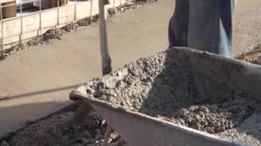 Bilinmeyen adamın orta kısmı kürek tutuyor inşaat alanındaki el arabasından beton döşeme kaldırımlarına beton döküyor.