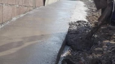 Bilinmeyen adamın orta kısmı kürek tutuyor inşaat alanındaki el arabasından beton döşeme kaldırımlarına beton döküyor.