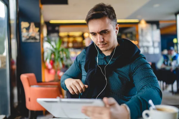 一人の若い大人の白人男性は一人でカフェに座っているデジタルタブレットとイヤホンポッドを使用しています — ストック写真