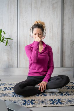 Yetişkin bir beyaz kadın milenyum kulaklıklarını internet rehberli meditasyon için kullanıyor. Evde gözleri kapalı zihin yogası yapıyor. Gerçek insanlar uzay özbakım kavramını taklit ediyorlar.