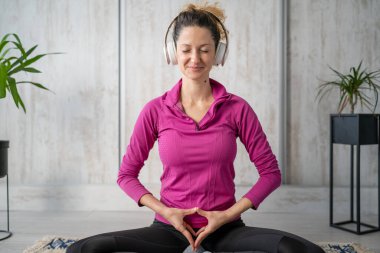 Yetişkin bir beyaz kadın milenyum kulaklıklarını internet rehberli meditasyon için kullanıyor. Evde gözleri kapalı zihin yogası yapıyor. Gerçek insanlar uzay özbakım kavramını taklit ediyorlar.