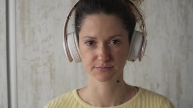 Yetişkin bir beyaz kadın milenyum kulaklıklarını internet rehberli meditasyon için kullanıyor. Evde gözleri kapalı, farkındalık yogası yapıyor. Gerçek insanlar kendi kendilerine bakıyorlar.