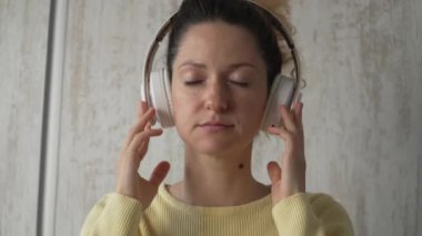 Yetişkin bir beyaz kadın milenyum kulaklıklarını internet rehberli meditasyon için kullanıyor. Evde gözleri kapalı, farkındalık yogası yapıyor. Gerçek insanlar kendi kendilerine bakıyorlar.