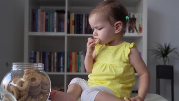 1人の赤ちゃんの女の子Caucasian幼児は家に座って ガラス瓶からクッキーを食べる子供時代のコンセプト屋内 — ストック動画