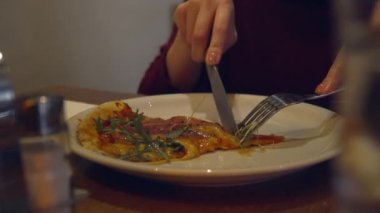 Karanlık bir restoranda çatal ve bıçakla yemek yerken tabaktaki pizza dilimini kesen kimliği belirsiz kadının ellerini kapatın.