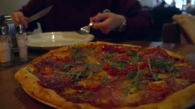 Karanlık bir restoranda çatal ve bıçakla yemek yerken tabaktaki pizza dilimini kesen kimliği belirsiz kadının ellerini kapatın.