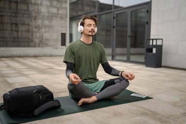 Genç, yetişkin, beyaz bir erkek, yoga ya da meditasyon için kapalı. Kulaklıkla dışarıda otururken iç huzuru ve denge kavramını gerçek insanlara uyguluyor.