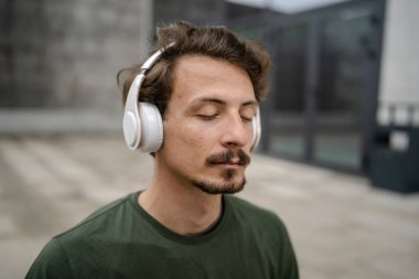 Genç, yetişkin, beyaz bir erkek, yoga ya da meditasyon için kapalı. Kulaklıkla dışarıda otururken iç huzuru ve denge kavramını gerçek insanlara uyguluyor.