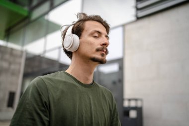 Genç, yetişkin, beyaz bir erkek, yoga ya da meditasyon için kapalı. Kulaklıkla dışarıda otururken iç huzuru ve denge kavramını gerçek insanlara uyguluyor.