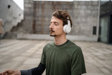Genç, yetişkin, beyaz bir erkek, yoga ya da meditasyon için kapalı. Kulaklıkla dışarıda otururken iç huzuru ve denge kavramını gerçek insanlara uyguluyor.