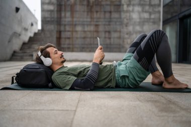 Genç, yetişkin, beyaz bir erkek, yoga ya da meditasyon için kapalı. Kulaklıkla dışarıda otururken iç huzuru ve denge kavramını gerçek insanlara uyguluyor.