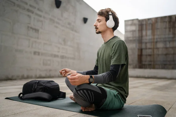 stock image One man young adult caucasian male eyes closed for guided training yoga or meditation while sitting outdoor with headphones self-care practice real people well-being inner peace and balance concept