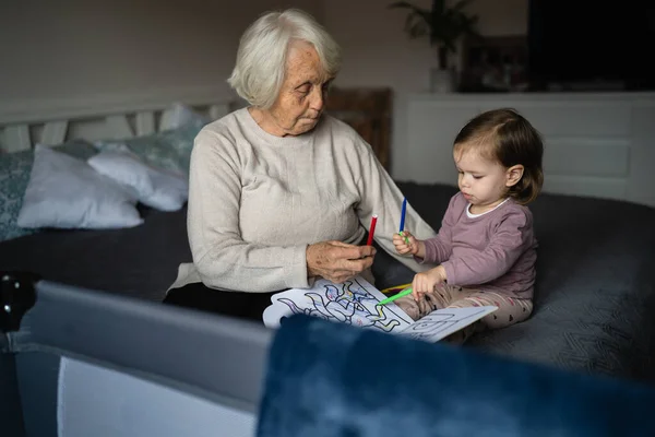 stock image Senior woman elderly caucasian pensioner old grandmother with small girl child toddler spending time together at home with books care and family concept growing up generation support real people